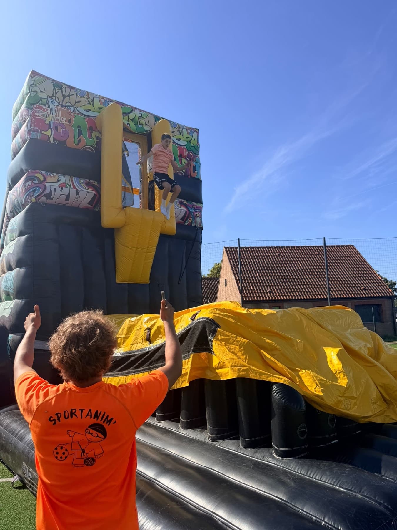 Animateur Sportanim' devant une structure gonflable dans une cour d'école.