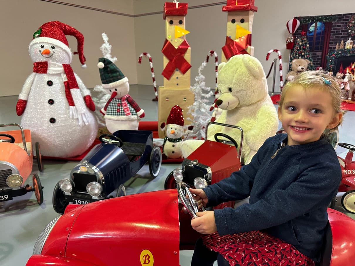 Enfant dans une petite voiture rouge au milieu des décors de Noël.